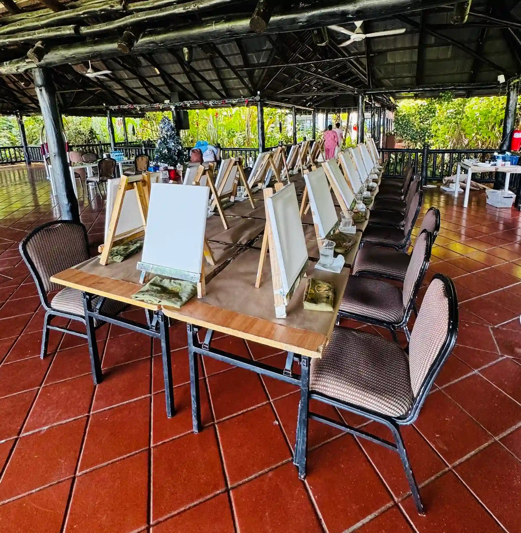 Rows of easels and canvases set up for a private group painting event under an open-air pavilion